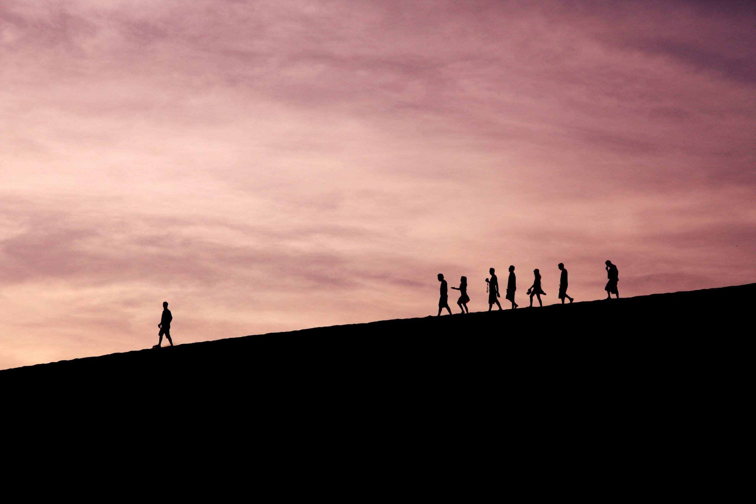 A person leads a group of people down a mountain at sunset
